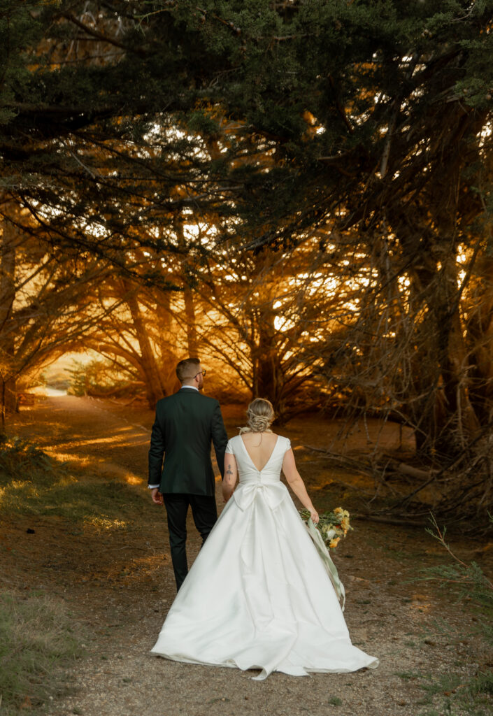 Bride and groom walking under trees at Garrapata State Park in Big Sur at sunset