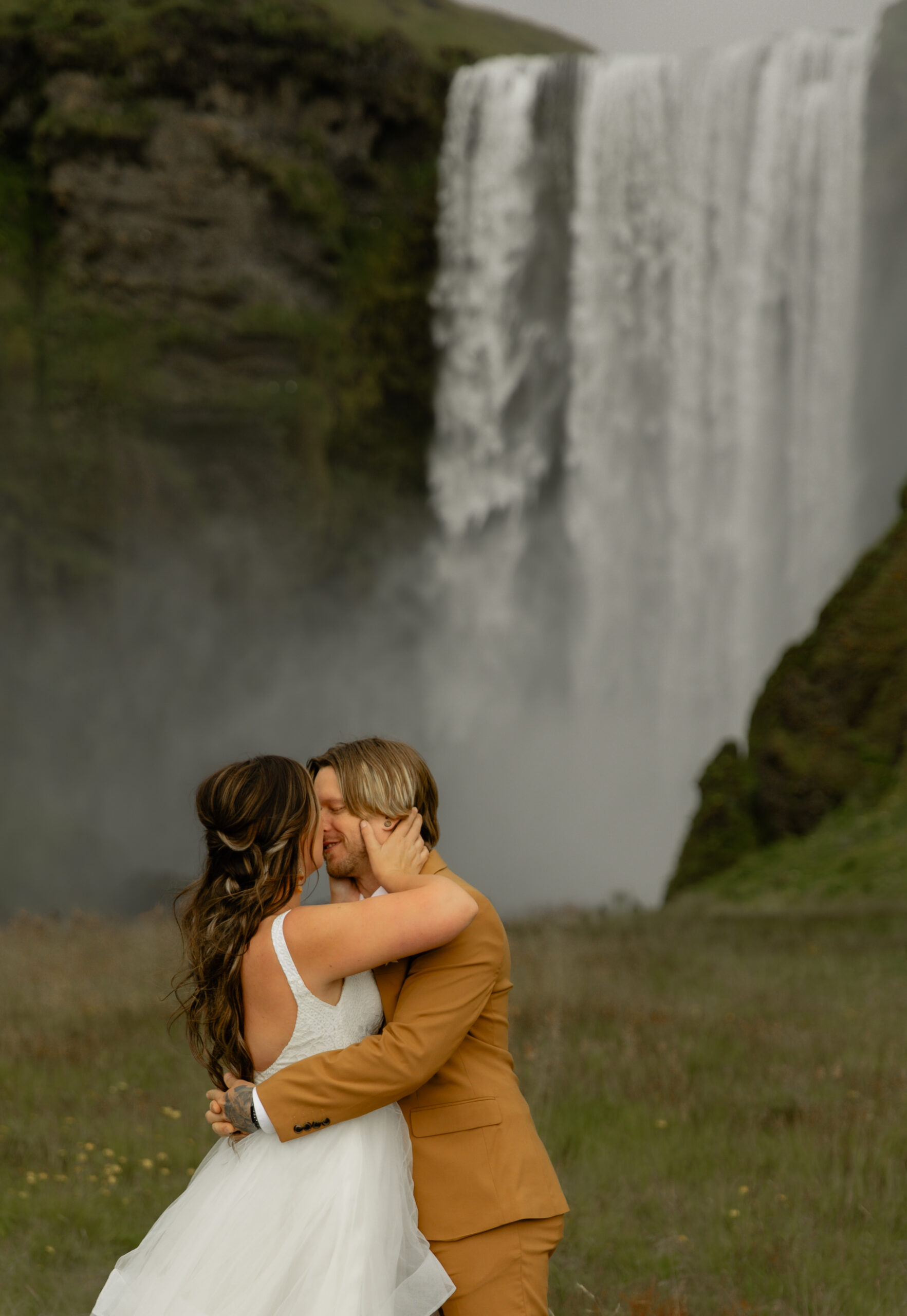 Bride and groom embracing in front of Skógafoss waterfall during Iceland elopement portraits
