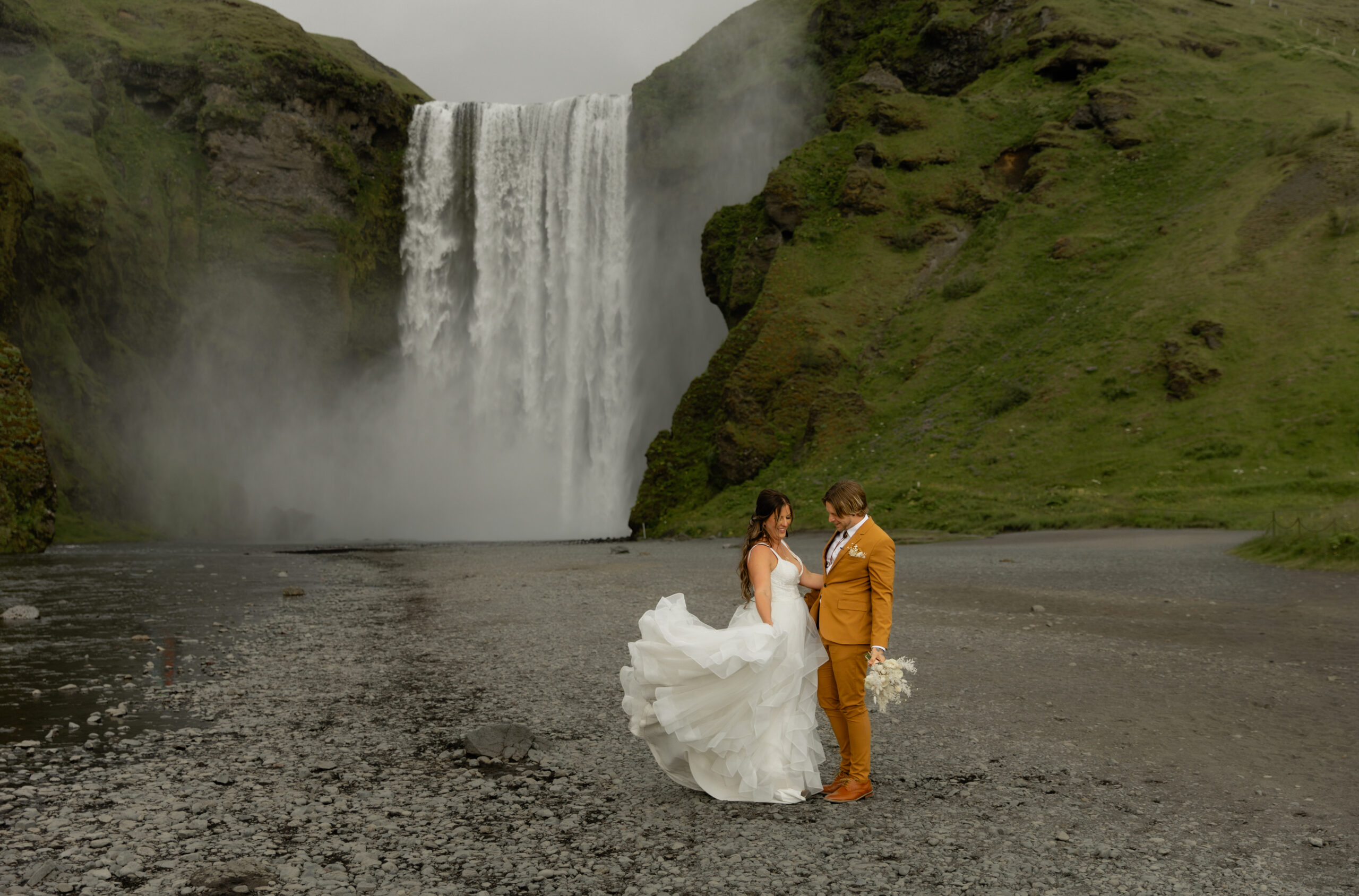 Wide portrait of bride and groom in front of Skógafoss waterfall during Iceland vow renewal