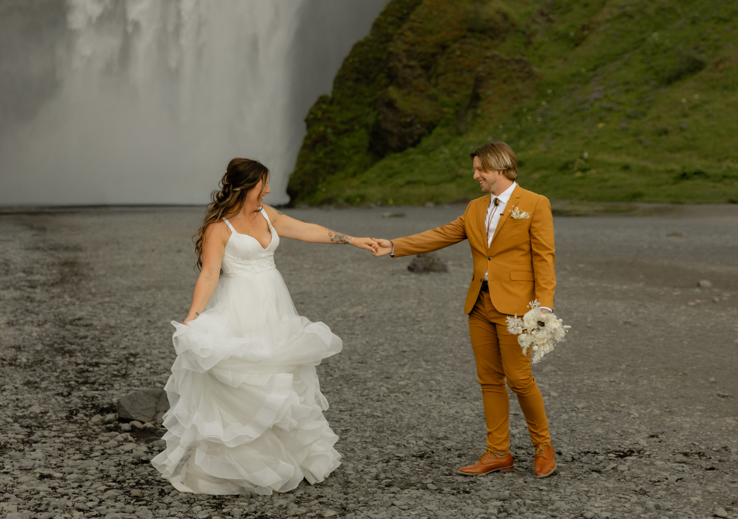 Bride and groom holding hands during portraits at Skógafoss waterfall in Iceland