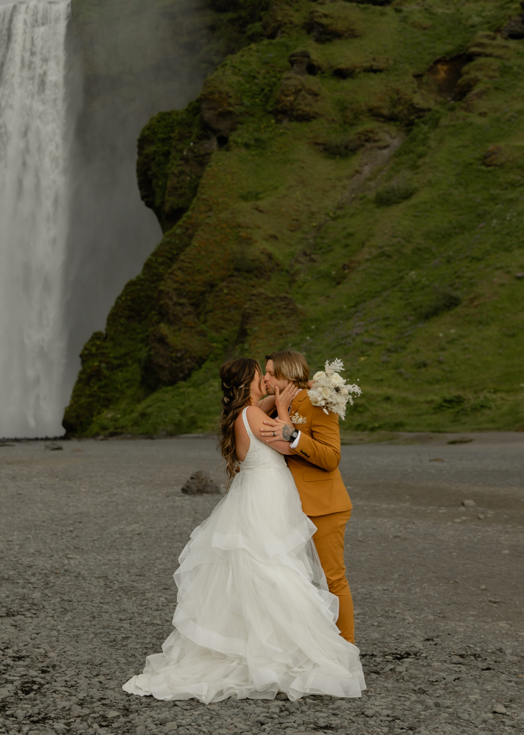 Bride and groom embracing near Skógafoss waterfall during Iceland vow renewal portraits