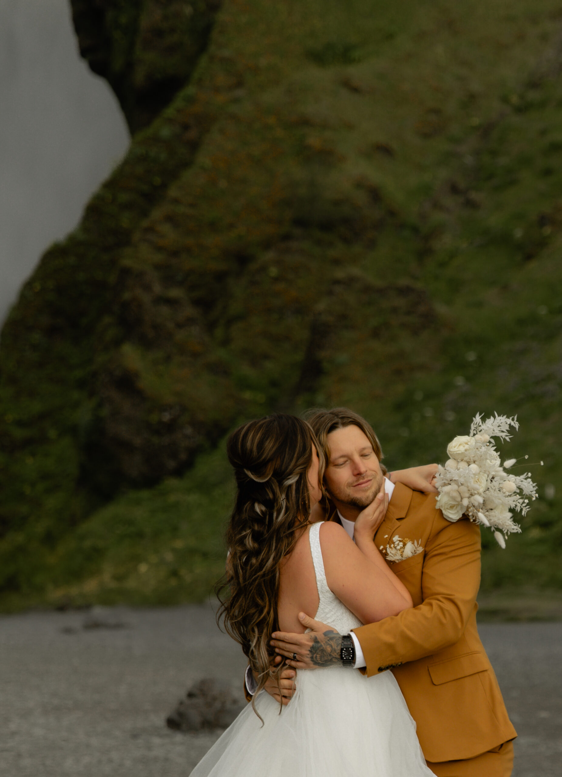 Bride and groom embracing during intimate Iceland vow renewal portraits beneath moss-covered cliffs