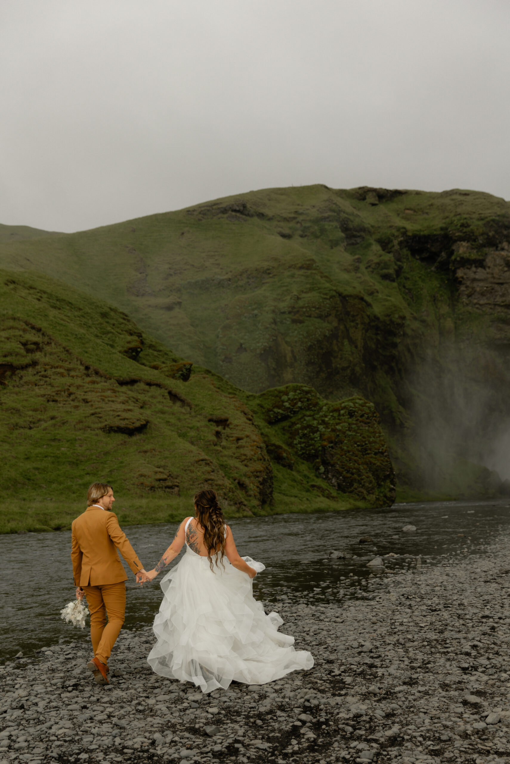 Couple walking beside Skógafoss waterfall during an intimate Iceland vow renewal