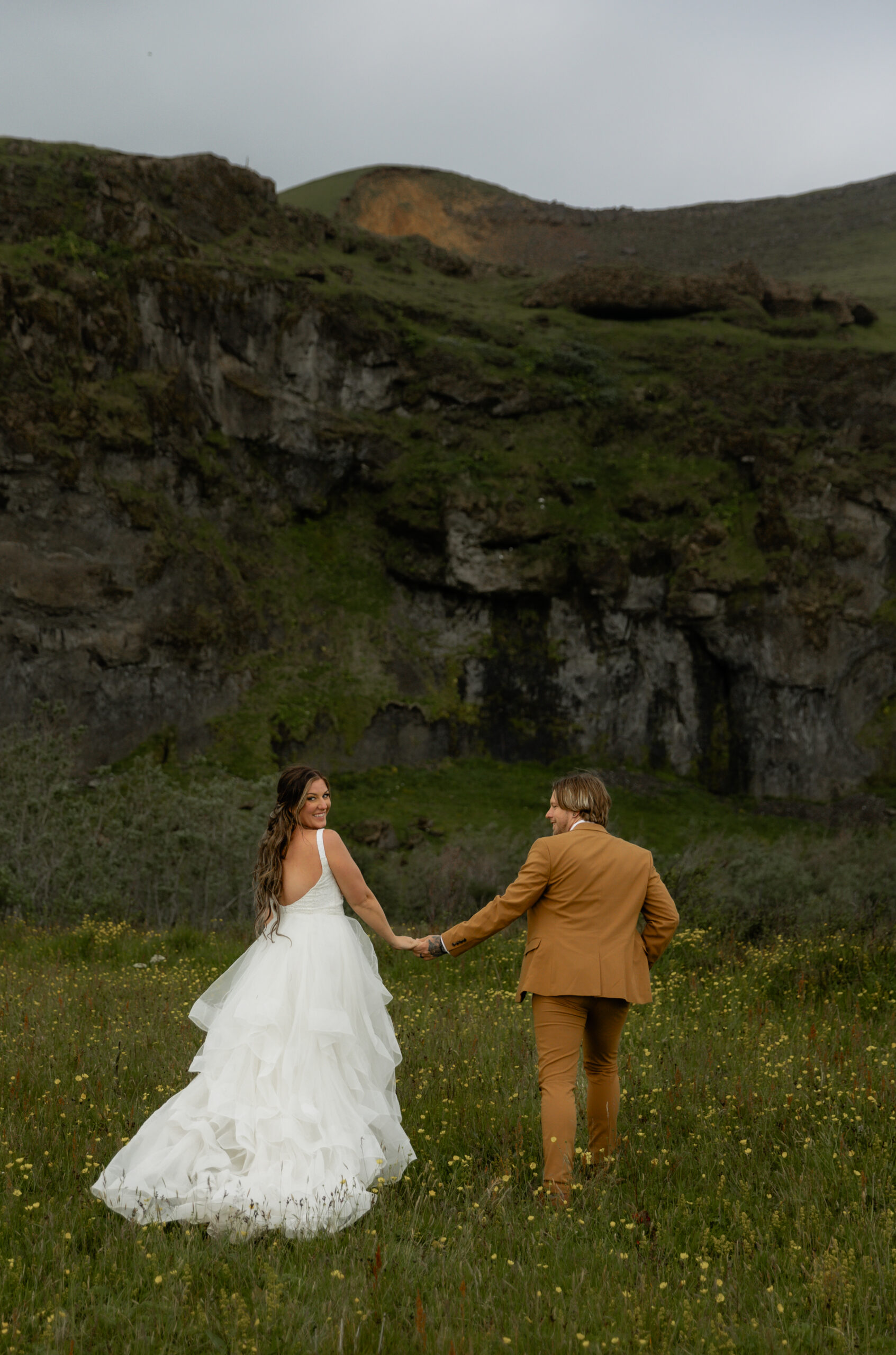 Bride and groom walking through wildflower meadow during Iceland vow renewal